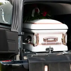 Biała trumna z wieńcem czerwonych róż w karawanie. Usługa transport zwłok powyżej 60 km.