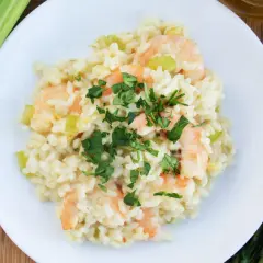 Kremowe risotto z krewetkami, ozdobione natką pietruszki, obok łodyg selera i oliwy.