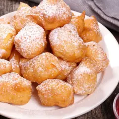 Une assiette de beignets banane saupoudrés de sucre glace, prêts à être dégustés avec une confiture de fruits rouges.