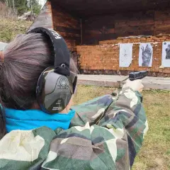 Strzelanie z broni na strzelnicy. Kobieta w słuchawkach ochronnych celuje z pistoletu do tarcz.