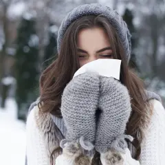 Femme en bonnet et moufles d'hiver se mouchant, un rappel pour prévenir le rhume.