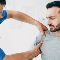 Fizjoterapeuta bada bark pacjenta, który odczuwa ból. Objawy uszkodzenia barku mogą być różne.
