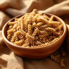 Drewniana miska pełna makaronu fusilli na lnianym tle.