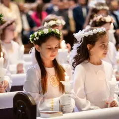 Dziewczynki w białych strojach z wiankami na głowach trzymają świece. Zastanawiasz się, ile kosztuje fotograf na komunie?