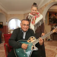 Don Vasyl siedzi z gitarą, obok niego stoi kobieta w chustce.