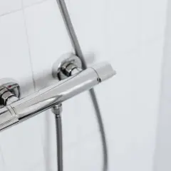 Chromowany panel prysznicowy na białej, kafelkowej ścianie. Idealny, gdy zastanawiasz się, jak zrobić prysznic na działce rekreacyjnej.