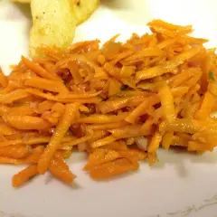 En fransk morotssallad med finstrimlad morot, lök och en lätt dressing. Serveras på en vit tallrik.