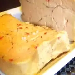 Deux blocs de foie gras sur une assiette blanche. L'un est parsemé de sel et de piment rouge, prêt pour une recette de foie gras au sel sans cuisson.