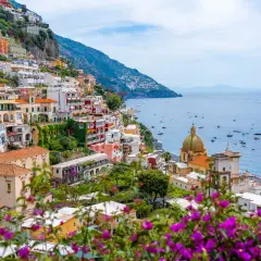 Colorful buildings cascade down a cliffside along the Amalfi road, overlooking a sparkling blue sea dotted with boats.