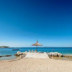 Słoneczna plaża z parasolem i leżakami w camping village Simuni. W tle wodny plac zabaw i spokojne morze.