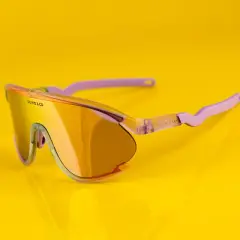 Oto odpowiedź na pytanie: jakie okulary na rower? Stylowe, pomarańczowe okulary sportowe z fioletowymi zausznikami, idealne na rowerową przejażdżkę.