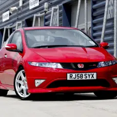 Czerwony Honda Civic Type R, wyglądający jak futurystyczne UFO, zaparkowany na torze wyścigowym.
