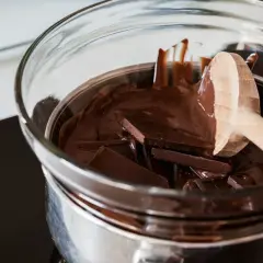 Trozo de chocolate oscuro derritiéndose en baño maría, con una cuchara de madera. Así es como derretir chocolate para postres.