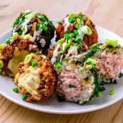Sechs bunte Onigiri mit verschiedenen Füllungen und Toppings, umgeben von Frühlingszwiebeln und Saucen.