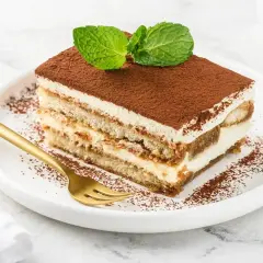 Pyszny kawałek tiramisu z mascarpone, posypany kakao i udekorowany miętą. Idealny sprawdzony przepis na deser.