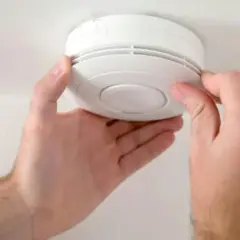 Ręce montują biały czujnik czadu na suficie.
