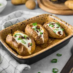 Drei gebackene Kartoffeln im Ofen, gefüllt mit Sour Cream und Speck. Garniert mit Schnittlauch.