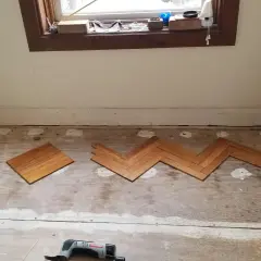 Wooden floor planks laid in a herringbone pattern on a subfloor, tools nearby. This is part of a project on how to level floor.
