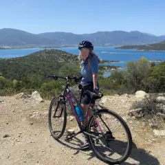 Woman on a bicycle enjoying scenic bicycle tours over 50, with a beautiful blue bay and mountains in the background.