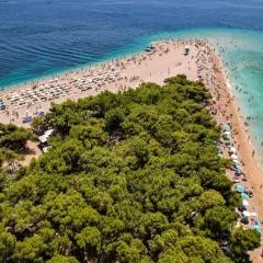 En solig strand med många parasoller och badande människor vid Zlatni Rat, en berömd udde på ön Brač i Kroatien.