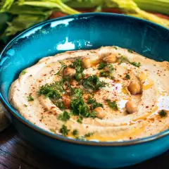 Cremiger Hummus mit Kichererbsen, Petersilie und Paprikapulver in einer blauen Schüssel, serviert mit Brot. Ein köstliches Hummus Rezept.