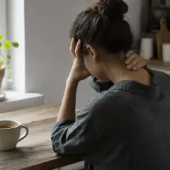 Donna con mal di testa, mani sulla testa e collo, accanto a una tazza di caffè. Forse la caffeina fa male.