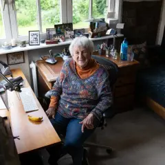 Ingrid Noll sitzt an ihrem Schreibtisch, umgeben von Erinnerungen und Inspirationen für ihre Geschichten über Kinder.