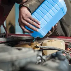 Mecánico vierte líquido refrigerante azul para limpiar radiador coche.