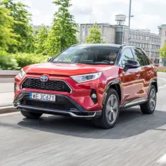 Czerwona Toyota RAV4 Hybrid w ruchu miejskim. Kierowca w okularach za kierownicą. Niskie toyota rav4 spalanie to atut tego SUV-a.