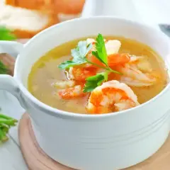 Aksamitna zupa krewetkowa z krewetkami i natką pietruszki, podana w białej miseczce.