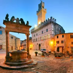 Piazza illuminata a Montepulciano, con pozzo rinascimentale, Palazzo Comunale e chiese. Perfetta per scoprire le cose da fare in zona.