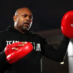 Roy Jones Jr. sweats during training, preparing for one of his best fights. He holds red boxing pads, ready to train.
