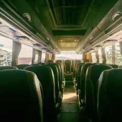 Wnętrze autobusu z rzędami ciemnych siedzeń i niebieskim oświetleniem podsufitowym.
