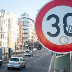 Verkehrsschild "Tempo 30 Berlin" auf einer Straße mit Autos und Gebäuden im Hintergrund.