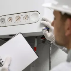 Technik w białej rękawiczce sprawdza piec gazowy, notując w zeszycie. Czy przegląd pieca gazowego jest obowiązkowy? Bezpieczeństwo przede wszystkim!