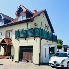 Jasny dom z balkonem i napisem "Ria" oferuje kwatery nad morzem. Biały samochód zaparkowany przed posesją.