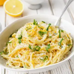 Un plat de pâtes au citron, garni de persil frais et de parmesan râpé, prêt à être dégusté.