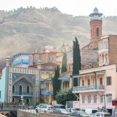 Kolorowe domy z balkonami i zdobioną fasadą meczetu w Tbilisi, stolicy Gruzji, na tle wzgórza.