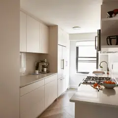 A modern galley kitchen makeover featuring sleek, handleless cabinets, a coffee machine, and a gas stove with a bowl of oranges.