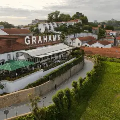Le vignoble Porto District, avec le nom "GRAHAM'S" en lettres blanches sur le toit, offre une vue sur des bâtiments traditionnels et des champs verdoyants.