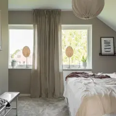 Mysigt sovrum med lågt snedtak. Sängen är bäddad med ljusa textilier, och två fönster ger utsikt över grönska. En tavla med texten "Ciao!" pryder väggen.