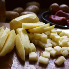 Skalade och skurna potatisar i olika former, redo för att bli härligt råstekt potatis. I bakgrunden syns hela potatisar och kött.
