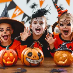 Tre barn med läskig ansiktsmålning och halloween-kostymer njuter av en halloween fest med pumpor och dekorationer.