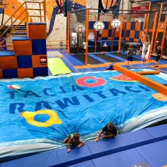 Wesołe skakanie na trampolinach w centrum rozrywki dla dorosłych. Dzieci i młodzież bawią się na wielkiej, niebieskiej macie z motywem basenu.