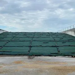 Ampia trincea agricola coperta da telo verde, con pareti in cemento e cielo nuvoloso.