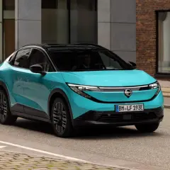 La Nissan Leaf 2026, in un vivace color acquamarina, sfreccia su una strada urbana, con un design futuristico che cattura l'attenzione.