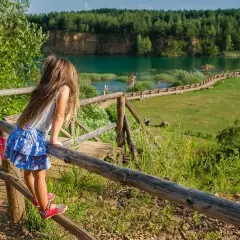 Dziewczynka na drewnianym pomoście podziwia Park Gródek Jaworzno. Cena wstępu jest niska, a widoki zachwycają.