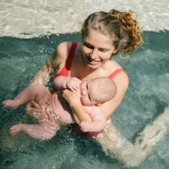 Mamma sorridente tiene in braccio il suo neonato durante un corso di nuoto per neonati in piscina.