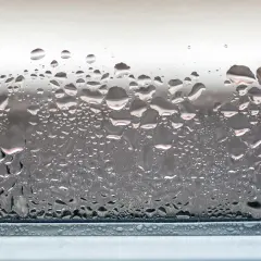Zaparowane okna po nocy, z kroplami wody tworzącymi na szybie wzory.