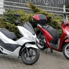 Dwa skutery, biały i czerwony, stoją na mokrym chodniku. Pytanie: co ile wymiana oleju w skuterze 50?